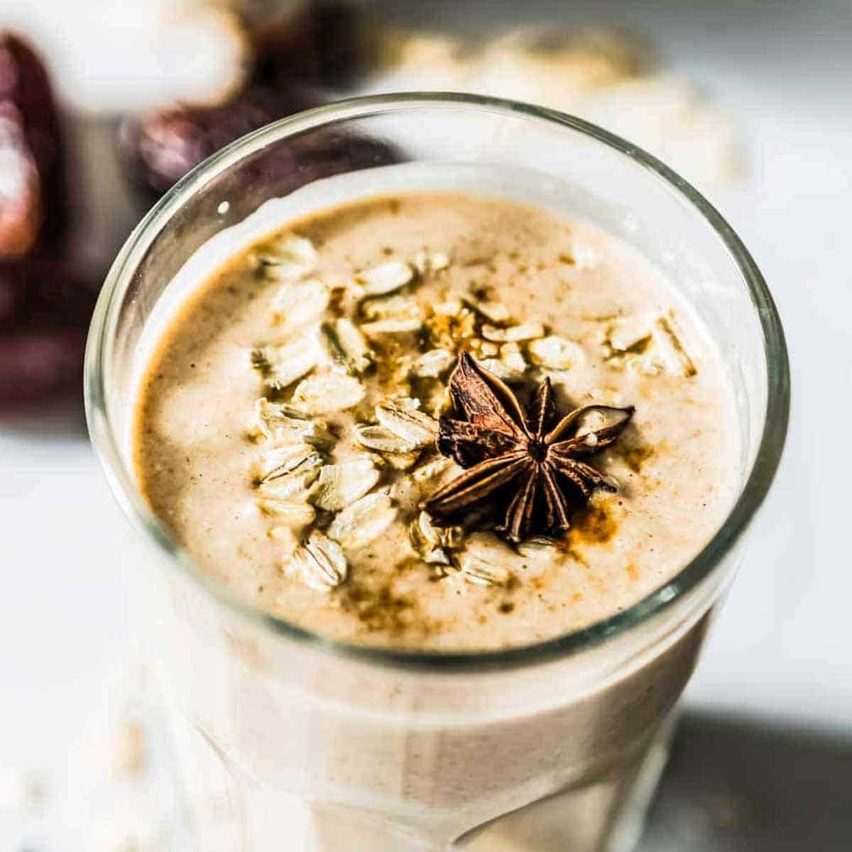 Cinnamon Date Smoothie, topped with oats and star anise, in a tall, clear glass.