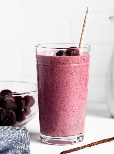 glass with pink diabetes smoothie topped with frozen cherries, a whole vanilla bean and a paper straw.