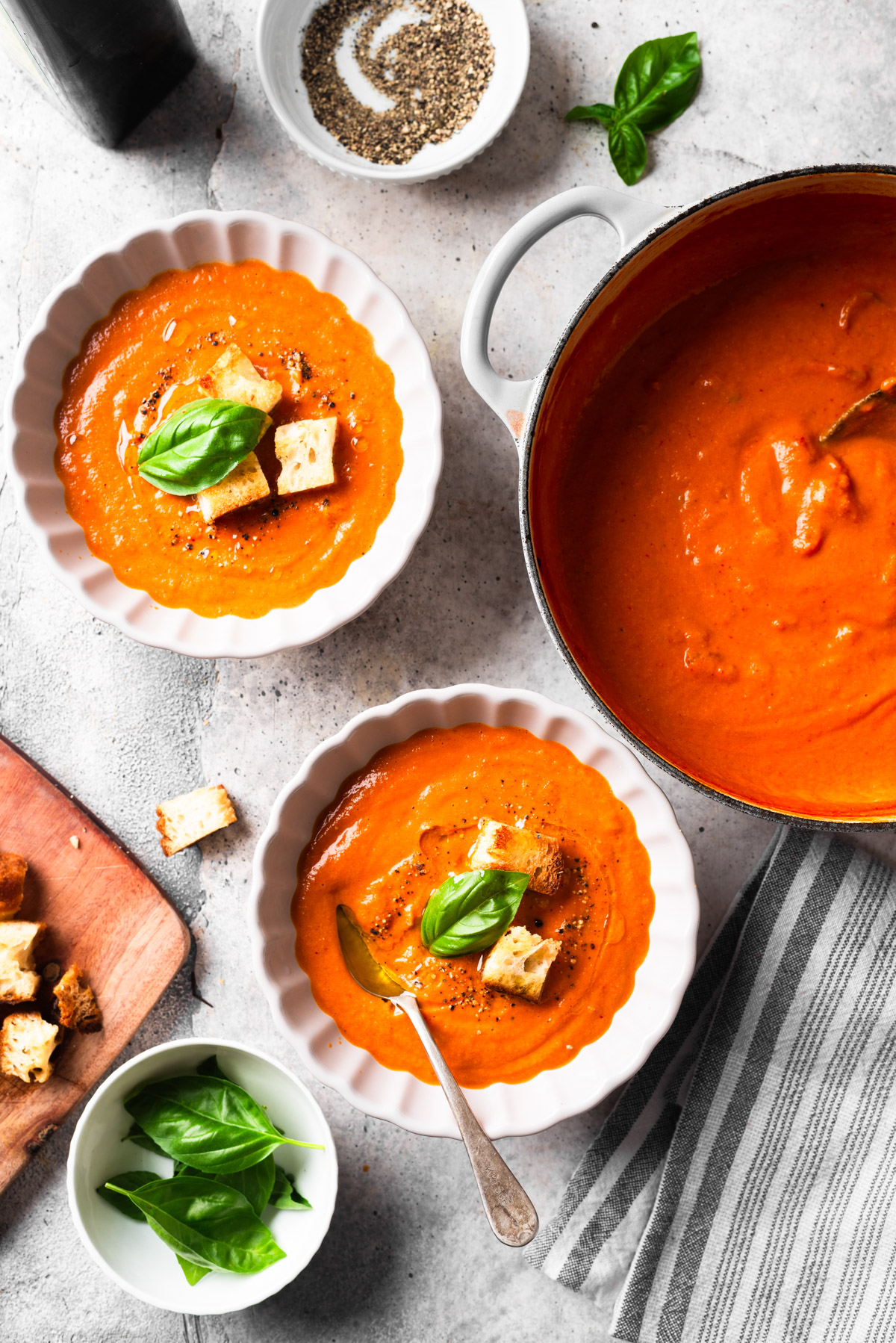 Pot of fire-roasted tomato soup on table with white bowls.