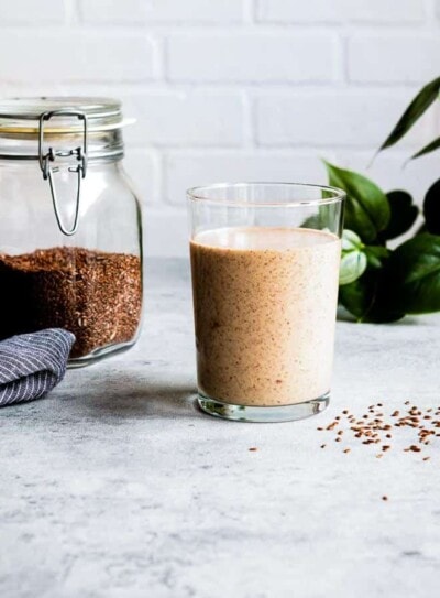 flaxseed smoothie in a glass next to a jar of flaxseeds.