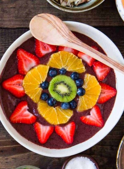 overhead photo of a fruit smoothie bowl topped with fresh fruit and a wooden spoon