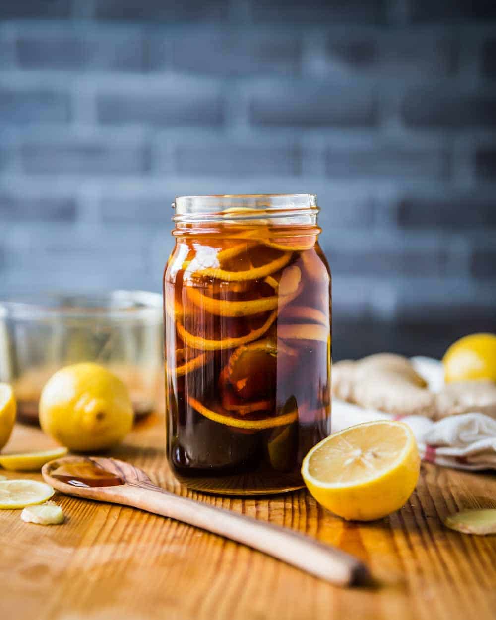 Ginger lemon honey tea for cough home remedy in a glass jar surrounded by sliced ingredients.