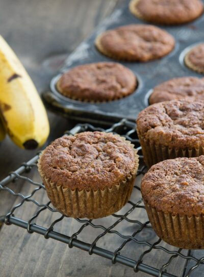 several gluten-free banana muffins on a cooling rack and in a muffin pan.