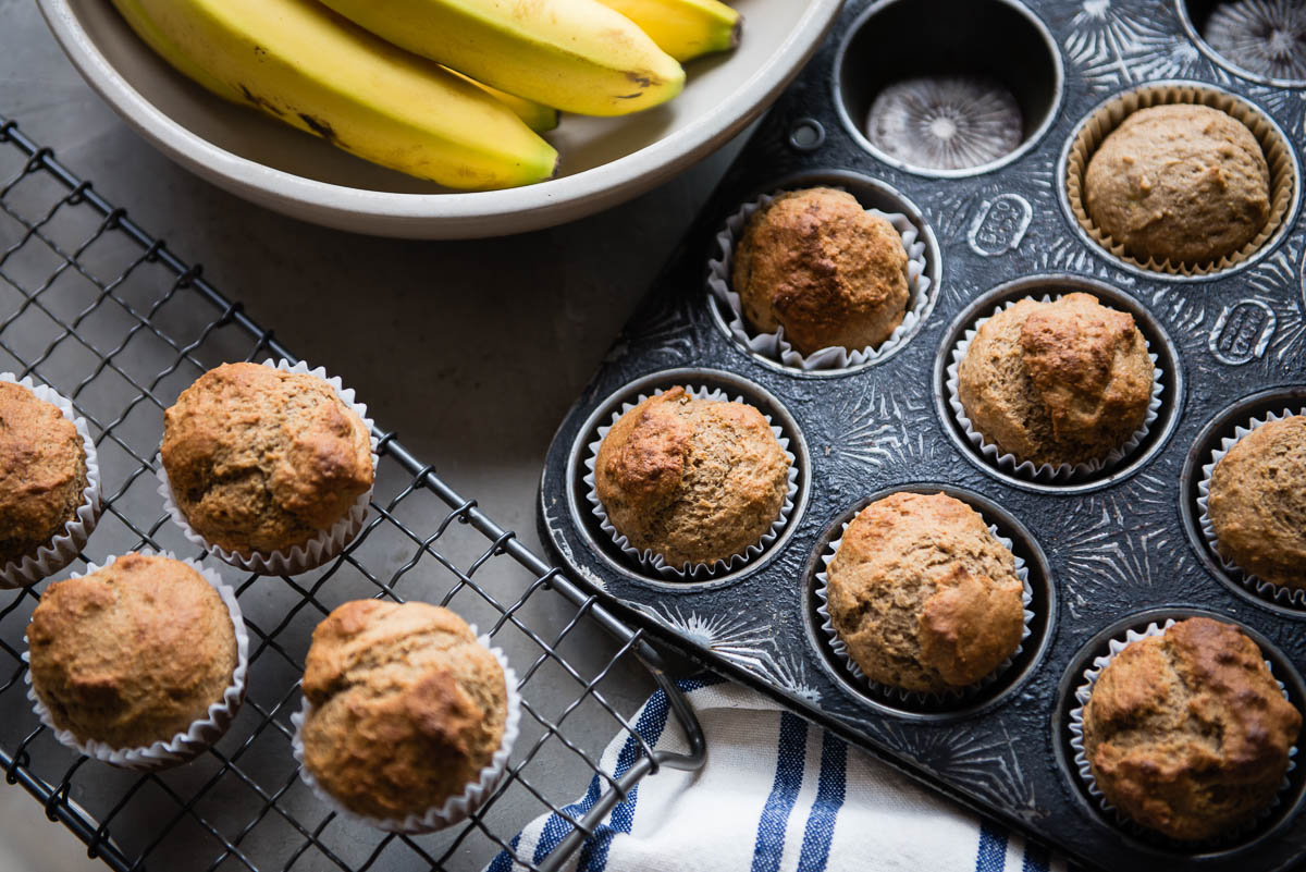 antique muffin pan full of muffin as well as a cooling rack with 4 baked muffins on it.