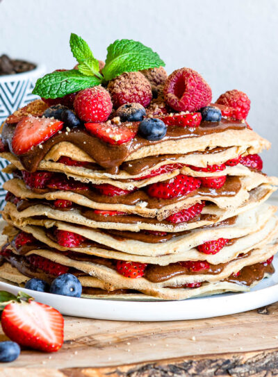 white plate of layered gluten free crepes filled with hazelnut chocolate spread and fresh fruit