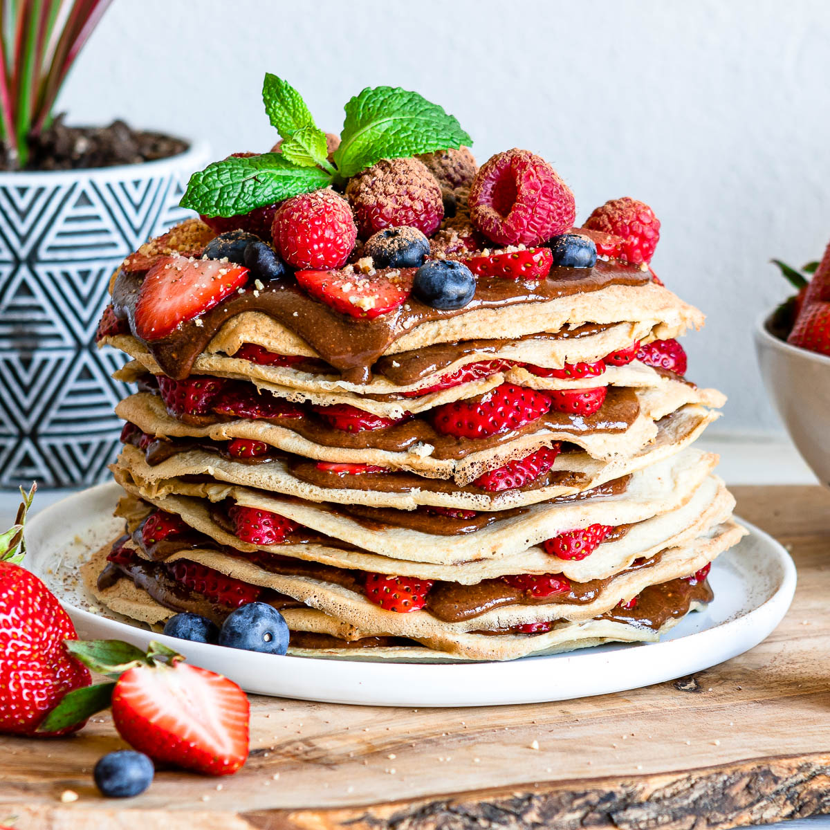 white plate of layered gluten free crepes filled with hazelnut chocolate spread and fresh fruit