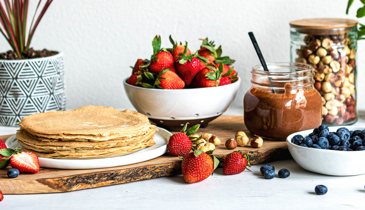 all the components for crepes ready to be put together, including chocolate hazelnut spread and fresh strawberries and blueberries