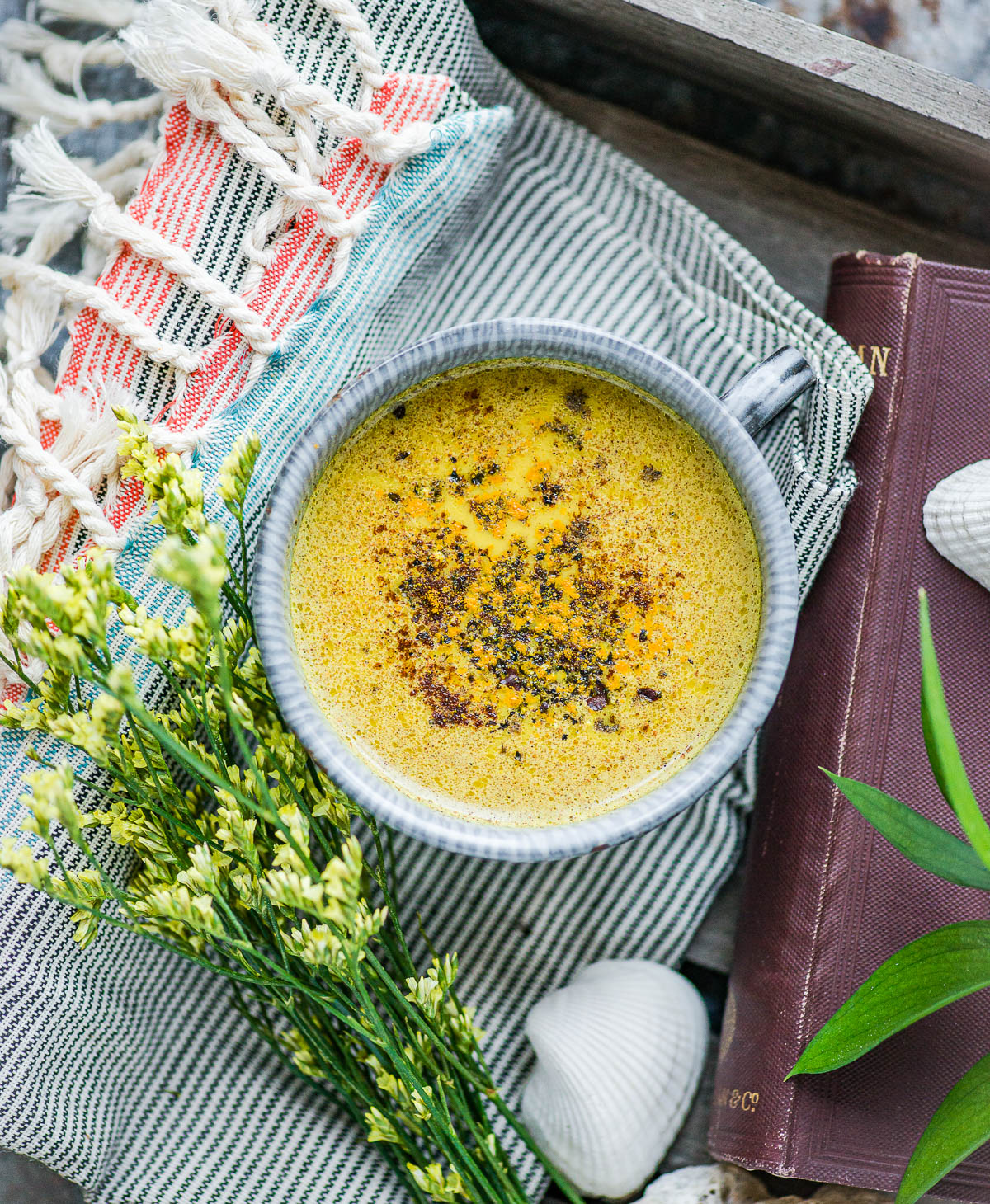 turmeric golden milk in a ceramic mug topped with turmeric and cracked black pepper, sitting on a tea towel. 