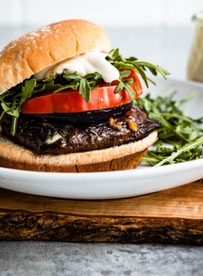 portobello mushroom burger on a white plate topped with arugula, sauce and tomatoes.