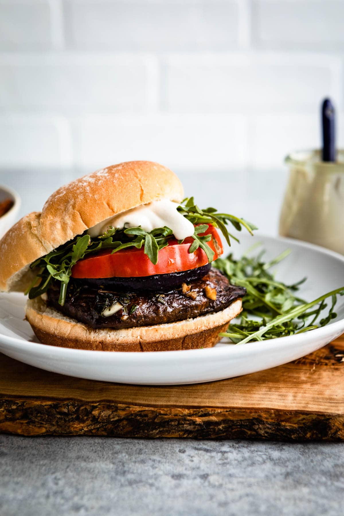 grilled portobello mushroom burger on a plate with tomato, arugula a vegan mayo.