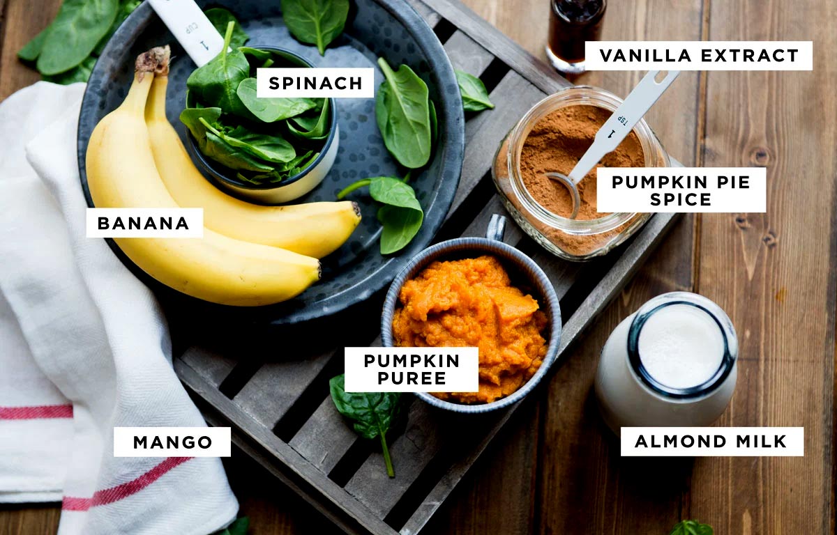 Labeled ingredients for a pumpkin smoothie recipe including spinach, vanilla extract, pumpkin pie spice, pumpkin puree, almond milk, banana and mango.