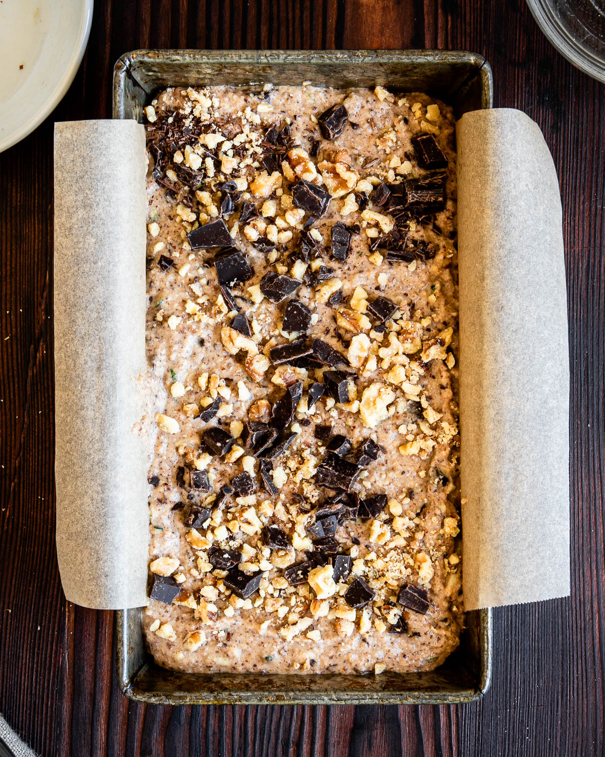 loaf pan with zucchini bread batter topped with chocolate chunks ready to be baked.