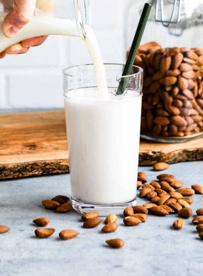 pouring fresh, homemade almond milk into a glass with a green straw.