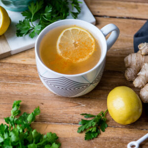 Mug with homemade detox tea recipe with fresh lemon, ginger root and parsley.