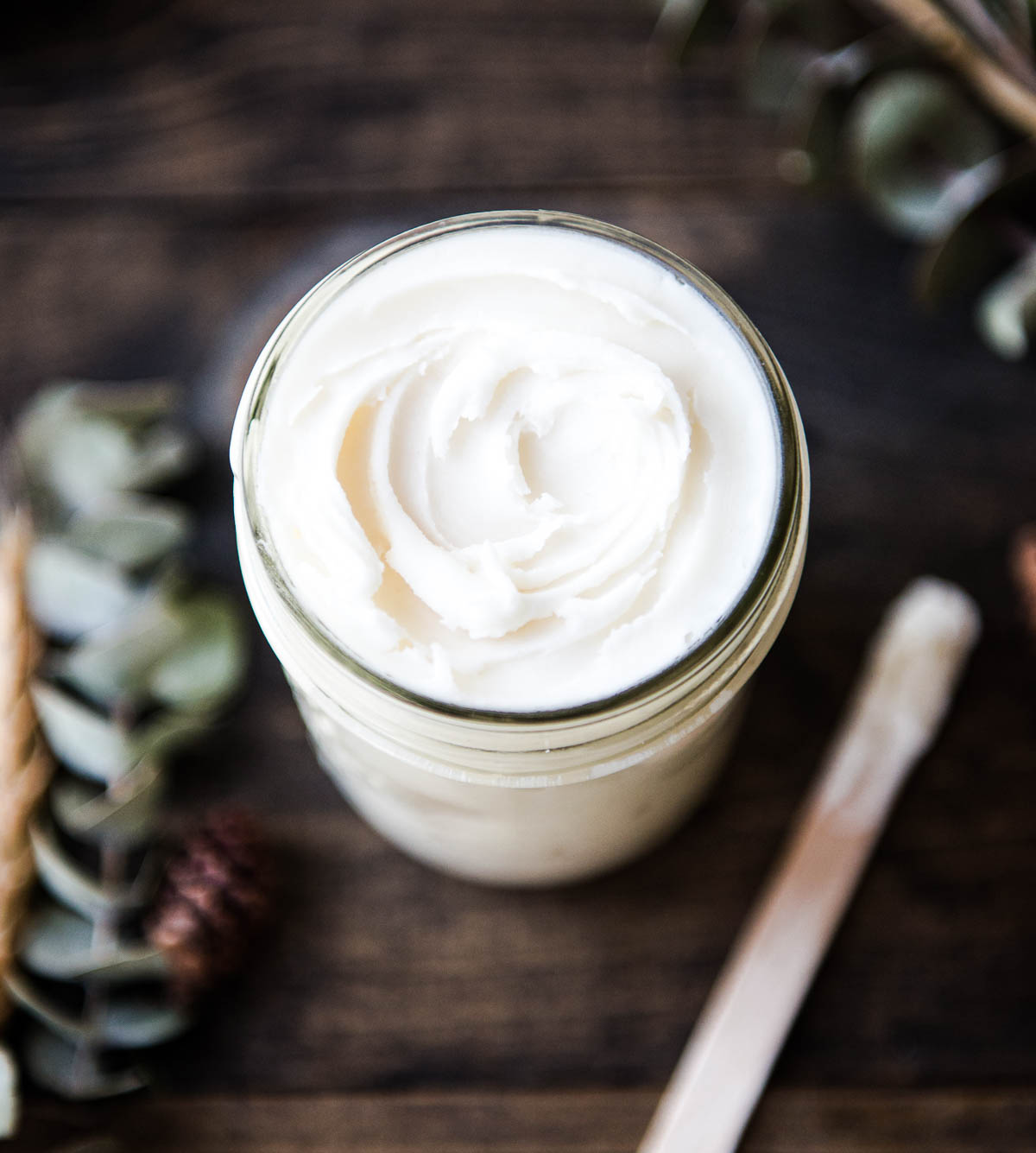 Glass jar of homemade deodorant made from a natural recipe with coconut oil and baking soda, alongside a wooden popsicle stick applicator.