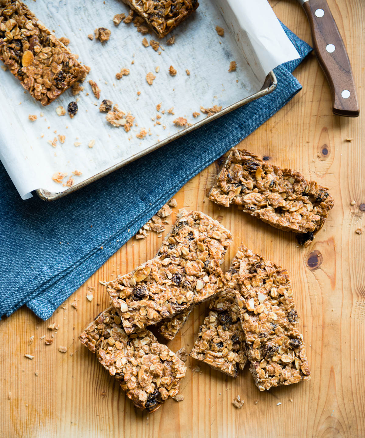 a pile of oatmeal raisin bars on a wooden counter top next to a blue tea towel.