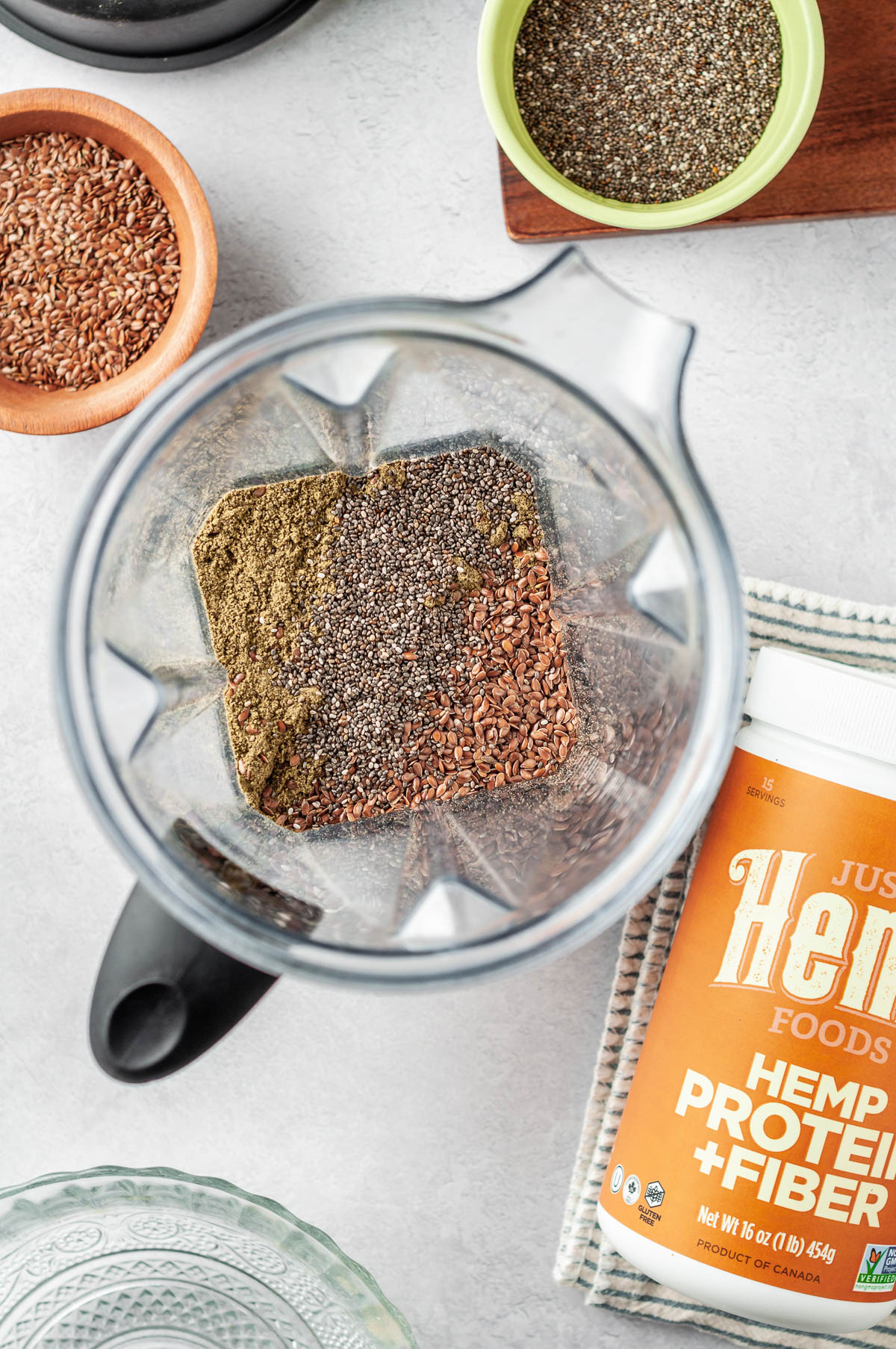 Overhead view of flax, chia, and hemp seeds in a blender, preparing to make homemade protein powder with added fiber.