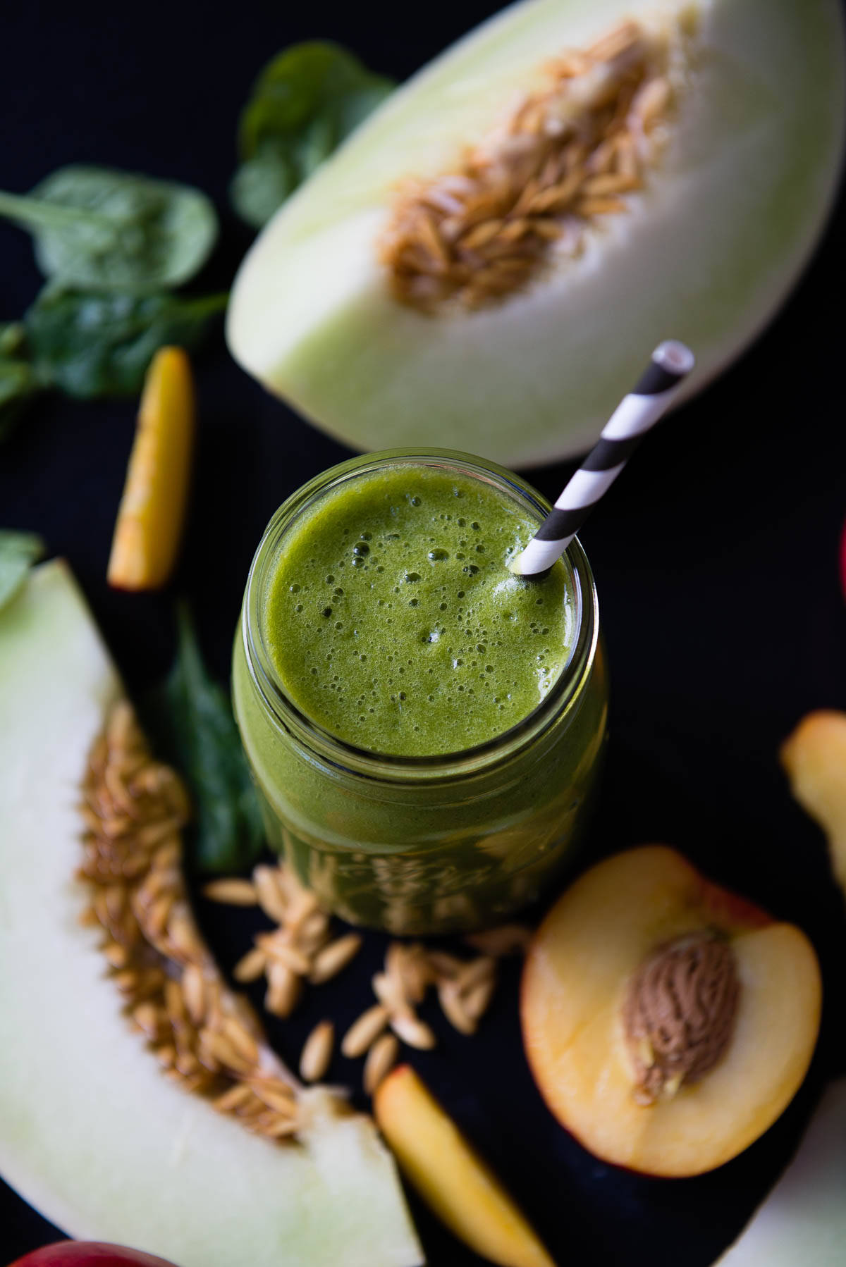 green smoothie in a glass jar with a black and white striped paper straw.