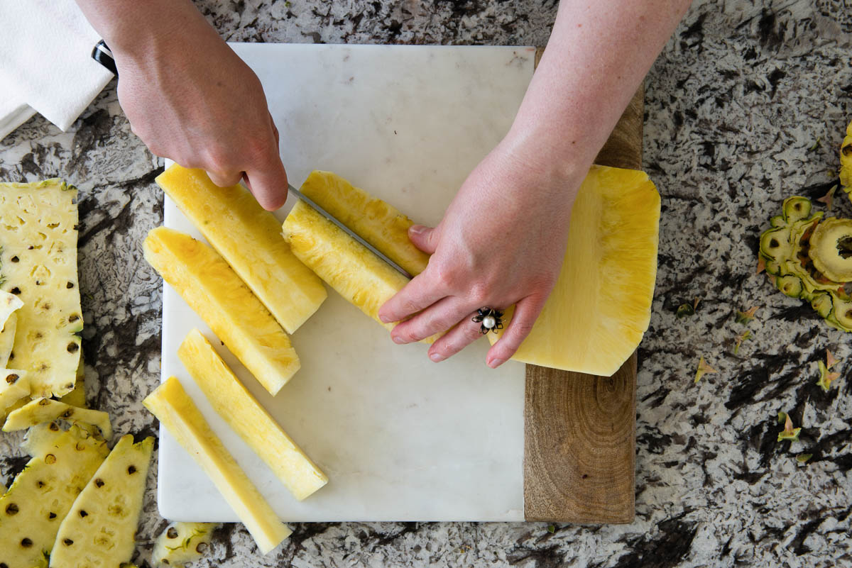 slicing long strips of fruit off the rind on a marble cutting board.