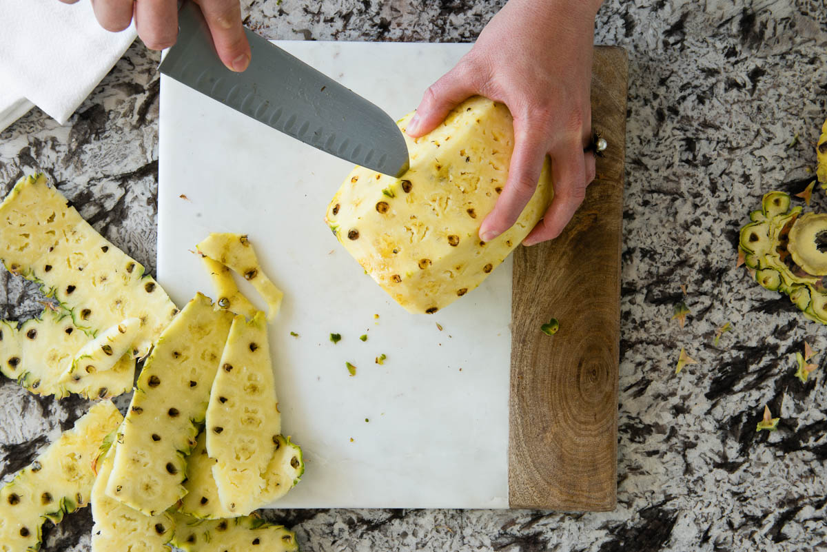 using a knife to remove eyes from a pineapple.