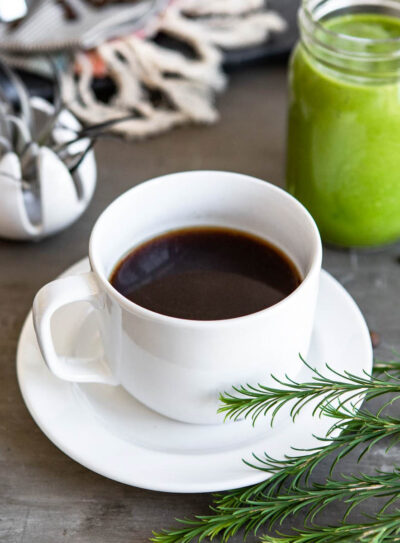 healthy coffee in a white cup on a white plate next to a jar of green smoothie.