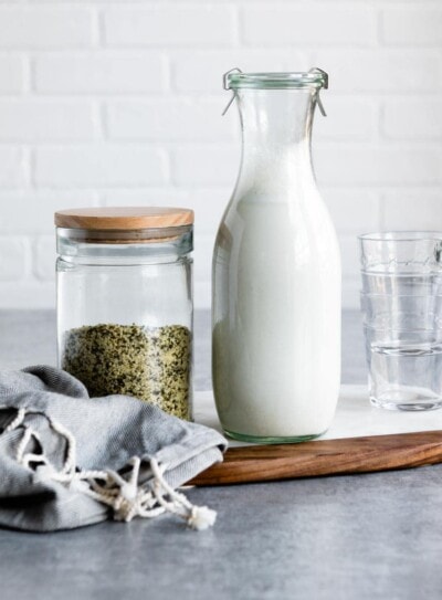 glass liter pitcher of homemade hemp milk next to a jar of hemp hearts.