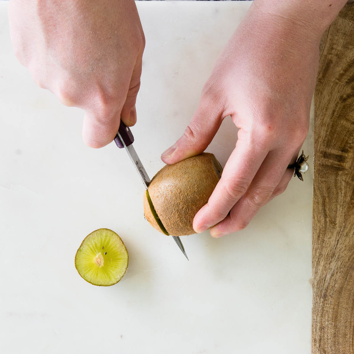 2 hands using a paring knife to cut the ends of a kiwi.