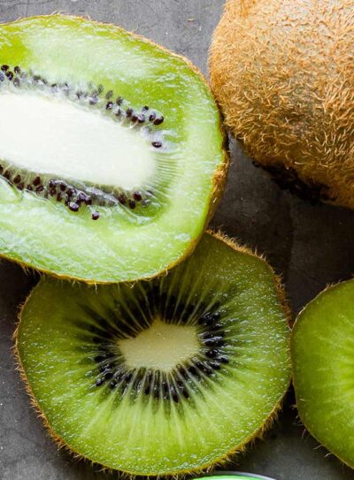 a kiwi cut in half lengthwise next to kiwi in slices next to a whole kiwi.