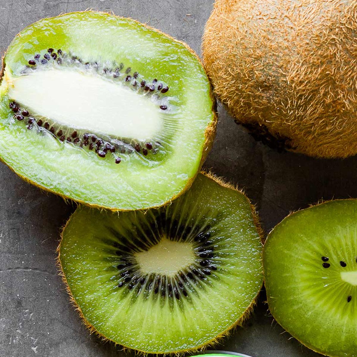 a kiwi cut in half lengthwise next to kiwi in slices next to a whole kiwi.