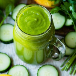 Bright green immune boosting smoothie in a glass jar, surrounded by fresh vegetables.