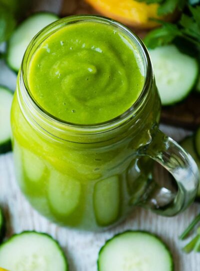 Bright green immune boosting smoothie in a glass jar, surrounded by fresh vegetables.