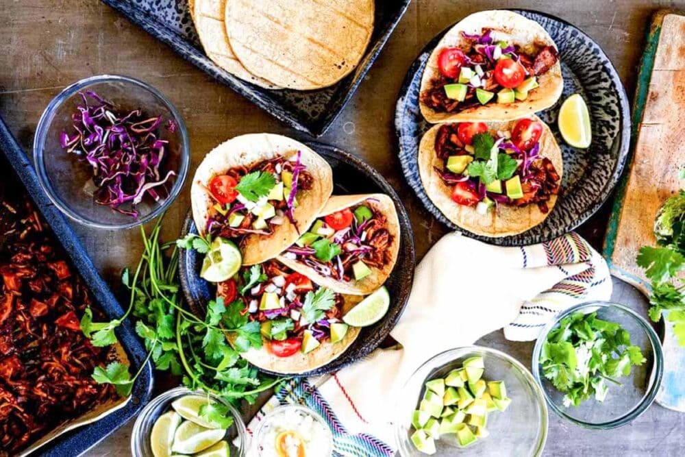 jackfruit tacos on plates with purple cabbage in a bowl.