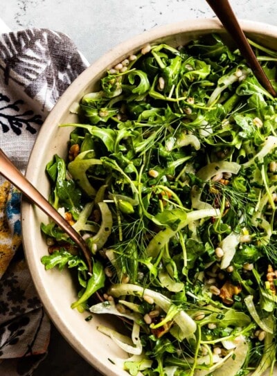 arugula salad. in a bowl with salad tongs.