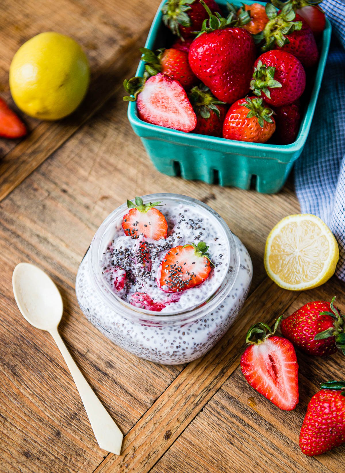 lemon strawberry chia pudding in a glass jar next to fresh lemons and sliced strawberries.