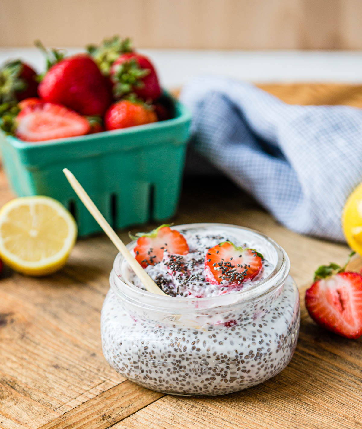 healthy snack recipe in a glass jar with a spoon surrounded by fresh strawberry slices and lemons.