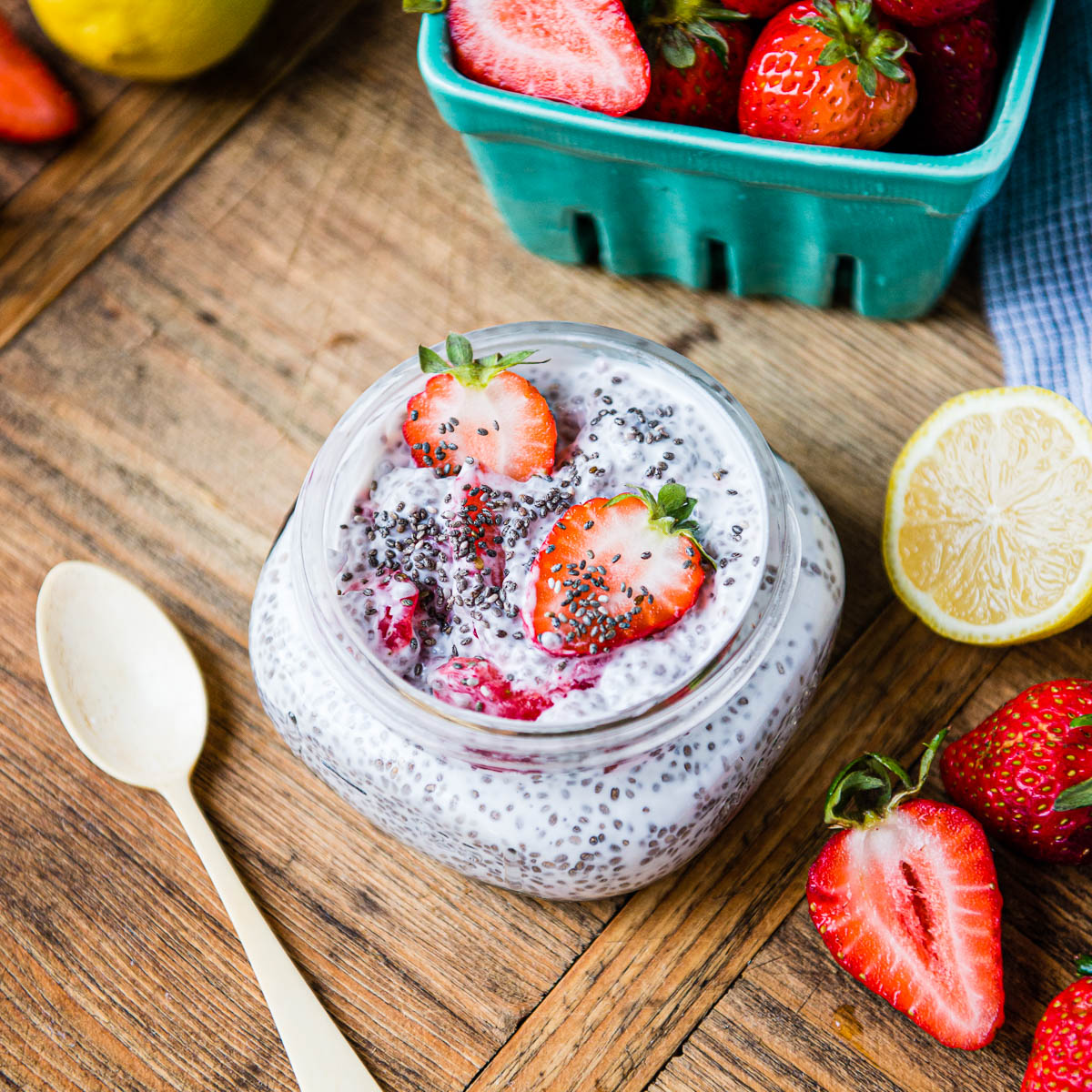 strawberry lemon chia pudding in a glass jar next to fresh lemons and sliced strawberries.