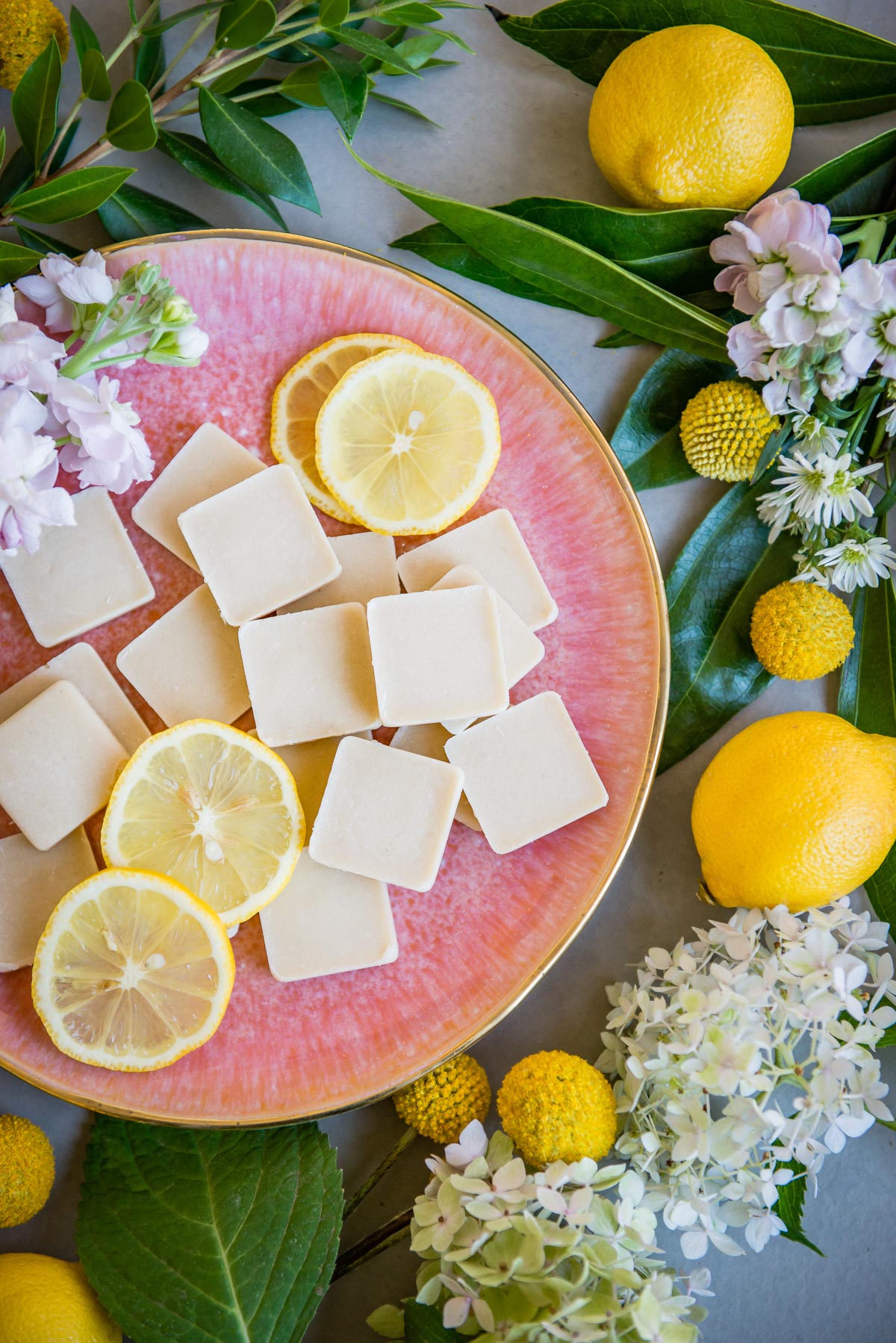 lemon fat bombs on a pink tray with cut and uncut lemons + mums surrounding it.