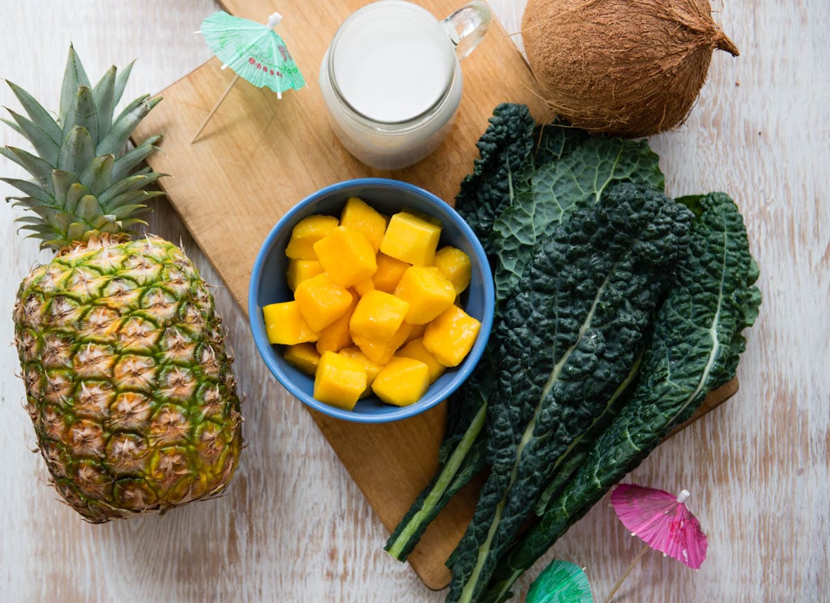 ingredients for a healthy, plant based snack including pineapple, mango, kale and coconut milk.