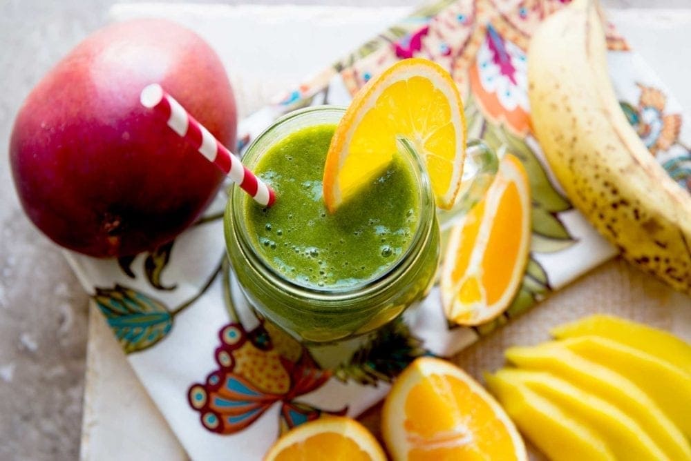 green smoothie in a glass jar with a red striped straw and an orange slice.