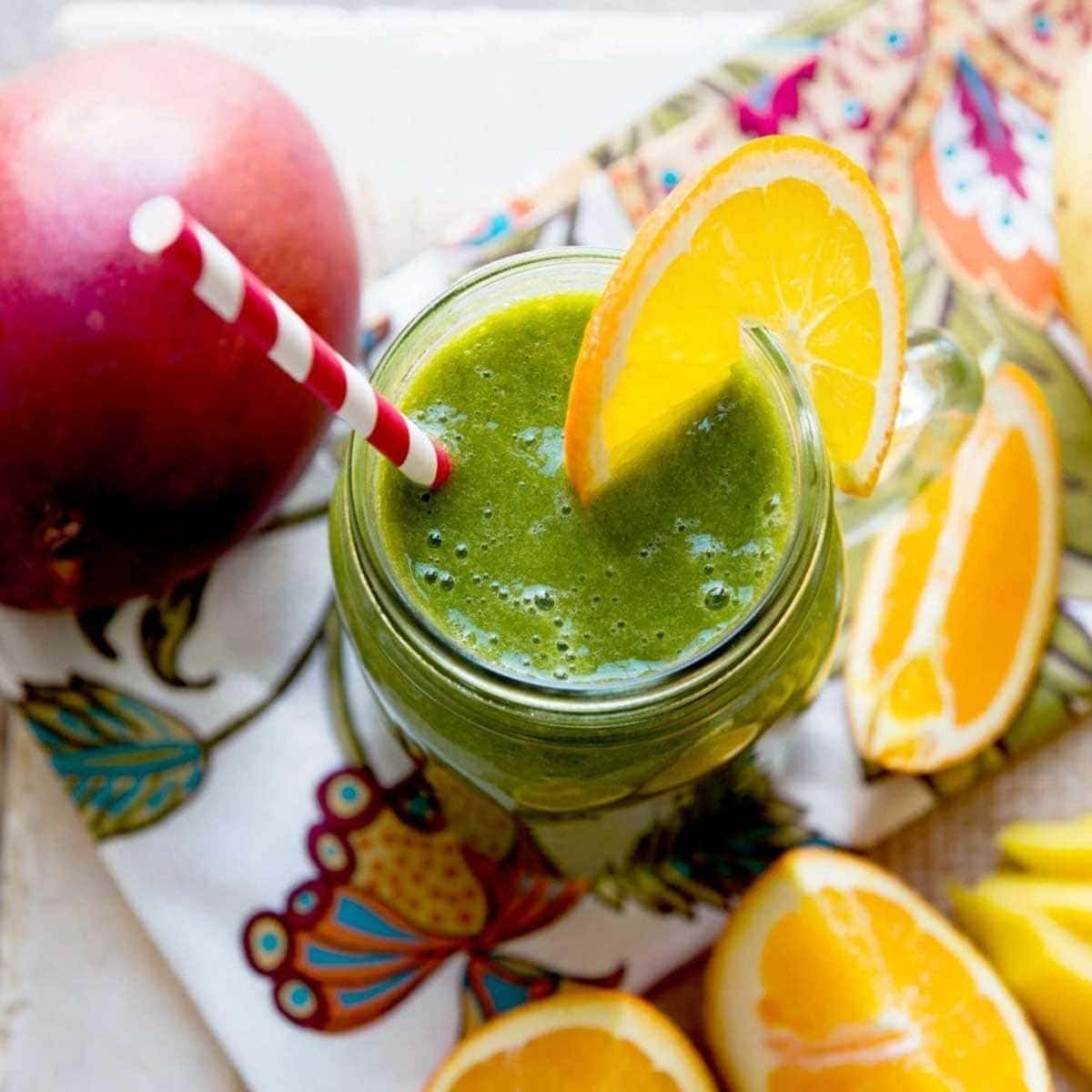 green smoothie in a glass jar with a paper striped straw and an orange slice on the rim.