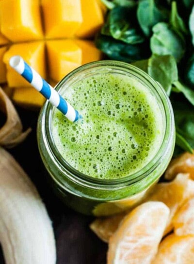 mango spinach smoothie in glass jar with blue and white striped paper straw.