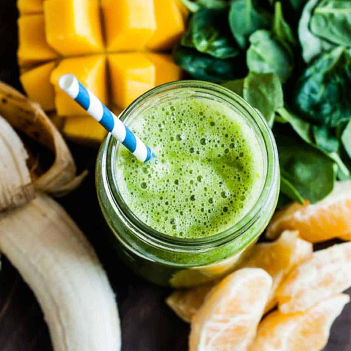 mango spinach smoothie in glass jar with blue and white striped paper straw.