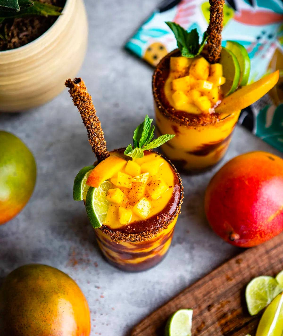 mangonada recipe in 2 glasses topped with fruit and tamarind straws.
