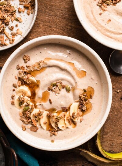 2 oat smoothie bowls topped with maple syrup and granola, next to a bowl of granola and banana.