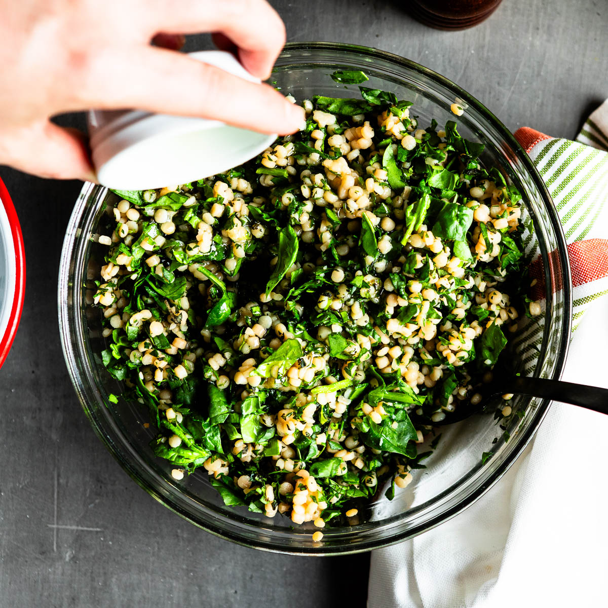 glass bowl of herbs, spinach and couscous.