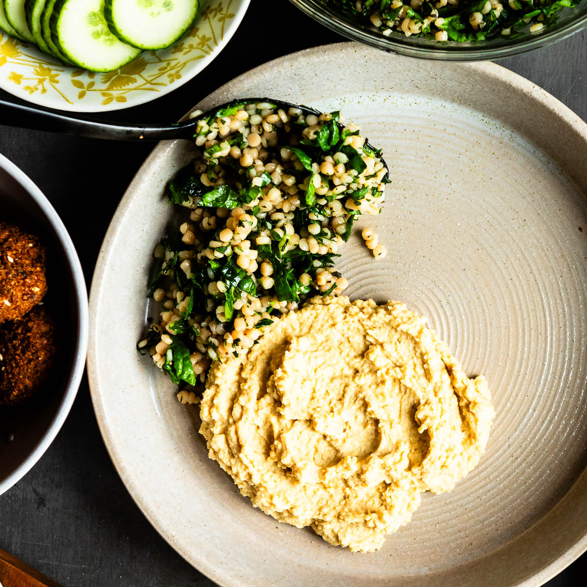 spooning herbed couscous onto a place next to some hummus. 