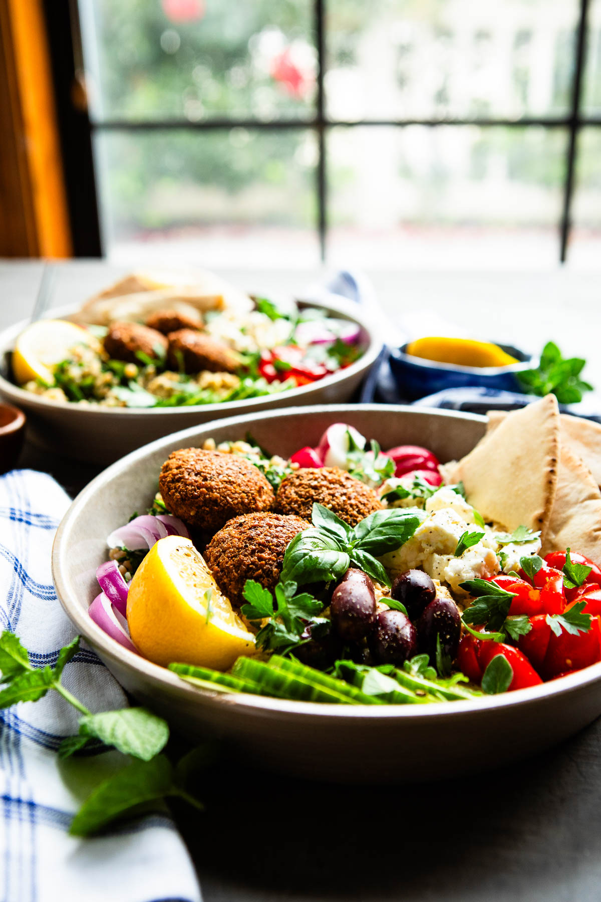 Mediterranean falafel salad bowl with vegetables and pita, sitting on a dining table. 