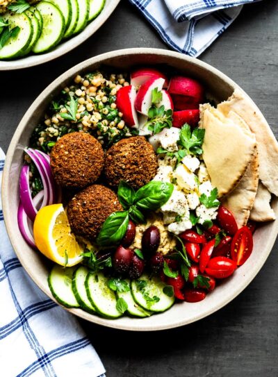 Mediterranean falafel bowl with fresh ingredients in a ceramic bowl on a concrete counter top.