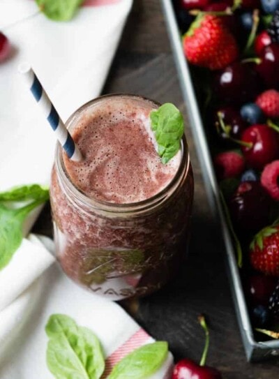 Mixed berry smoothie in a glass jar with a paper straw, next to a container of fresh mixed berries.