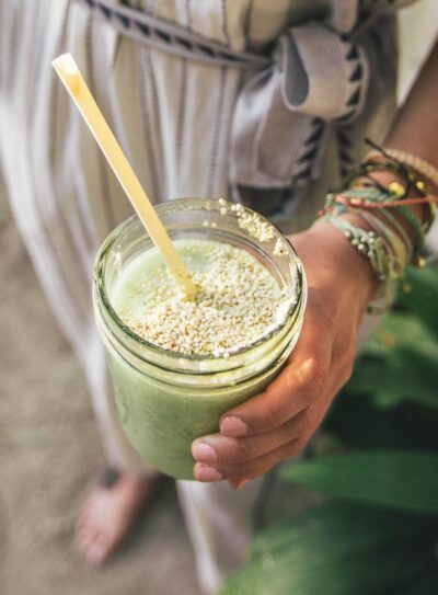 banana free smoothie in glass jar with straw held by hand.